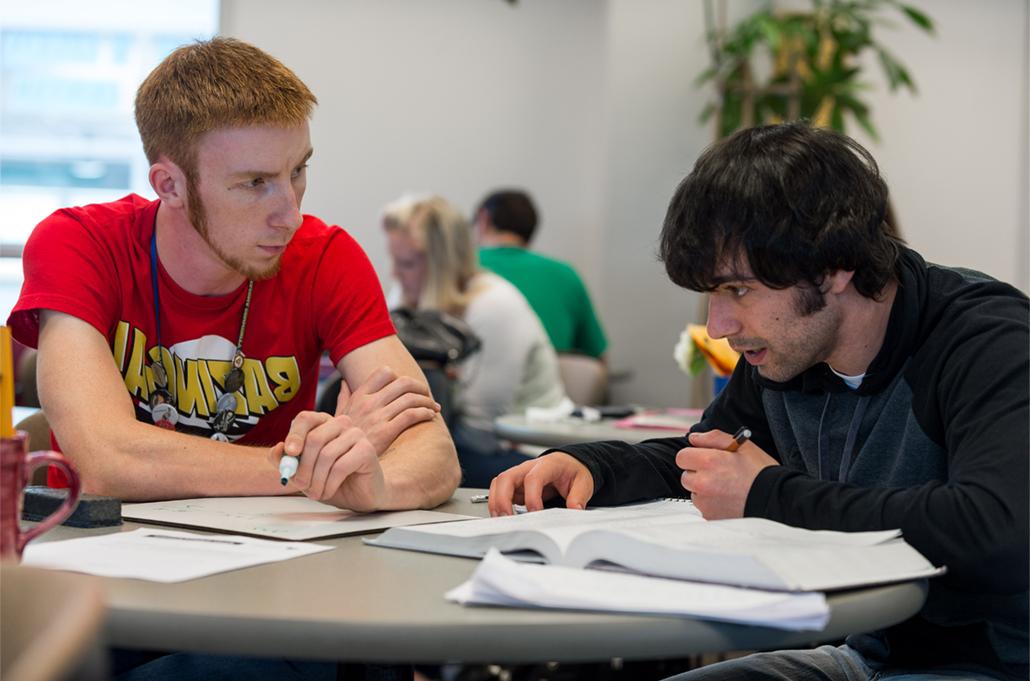 A student and a tutor sit at a table discussing chemistry.